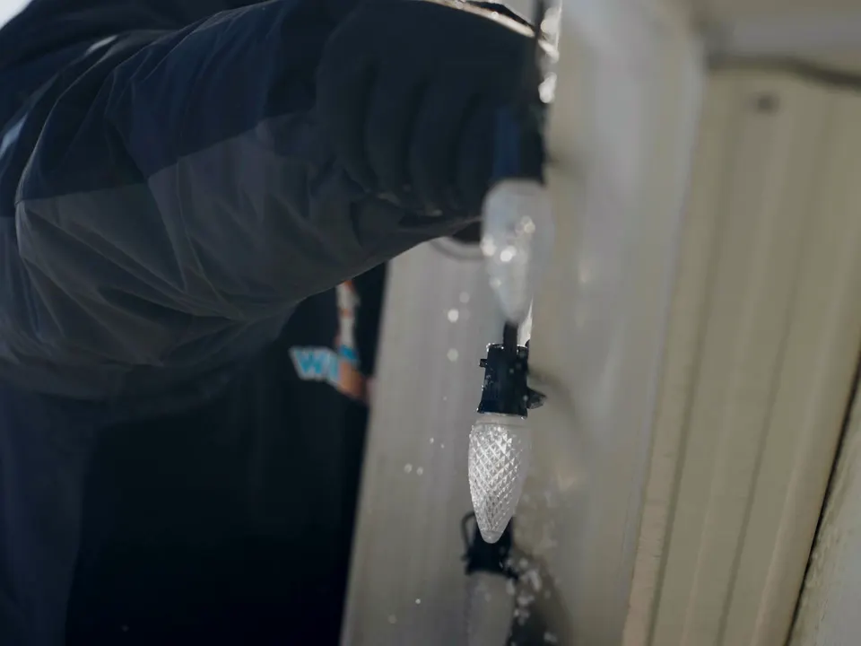 A Winducks installer’s gloved hand at the gutter with a strand of C9 bulbs