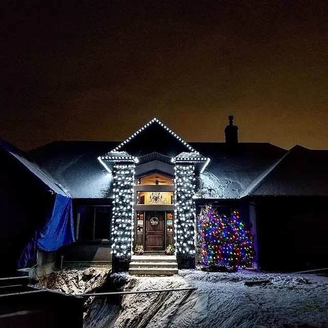 White Christmas lights on a front gable and wrapped entry pillars, with a multicolour tree beside the door