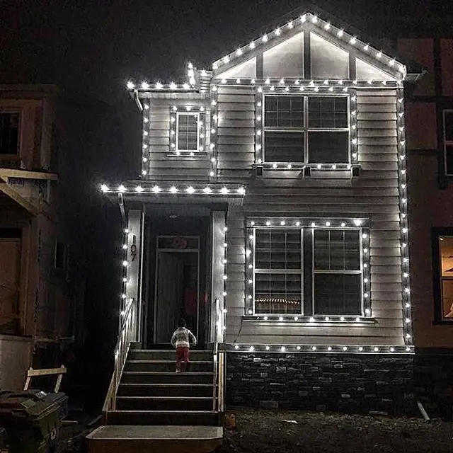 Cool white Christmas lights outlining the roofline, windows and front steps of a two-storey home