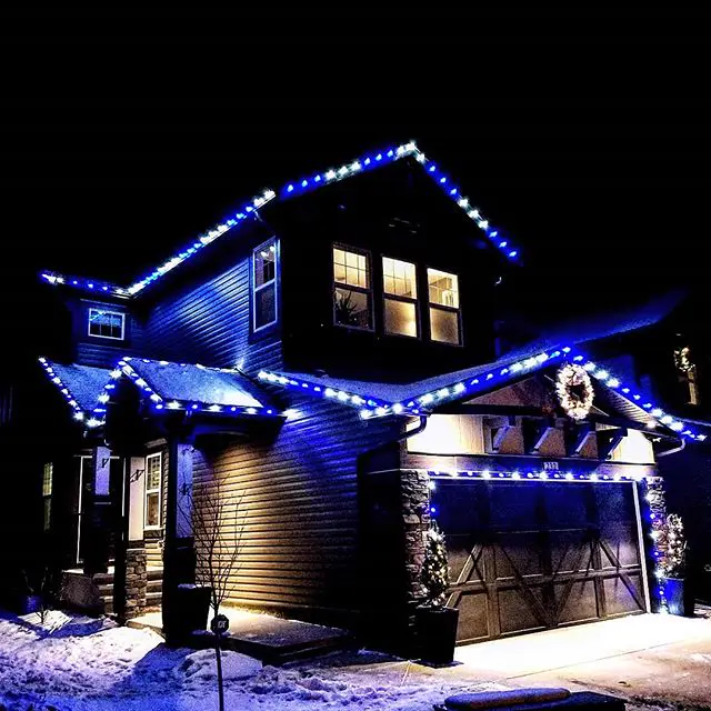 Blue and white roofline Christmas lights on a two-storey home with a lit wreath