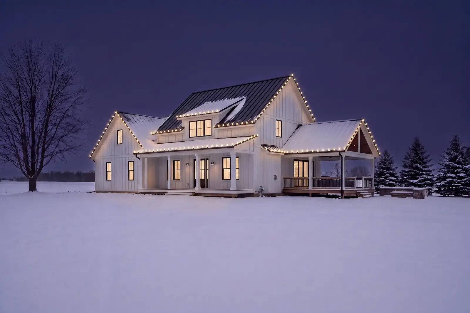A white farmhouse in a snowy field at dusk with warm white Christmas lights on every roofline